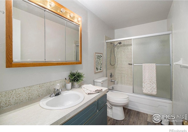 full bathroom with wood-type flooring, a textured ceiling, combined bath / shower with glass door, toilet, and vanity