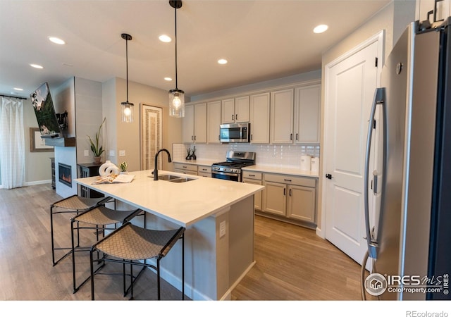 kitchen featuring an island with sink, appliances with stainless steel finishes, light hardwood / wood-style flooring, sink, and decorative light fixtures