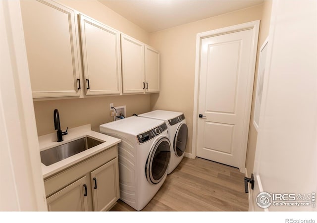 laundry area with light hardwood / wood-style flooring, independent washer and dryer, cabinets, and sink