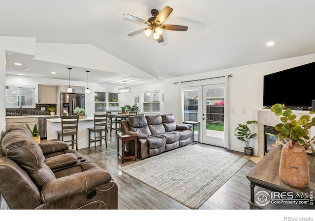 living room featuring lofted ceiling, french doors, a tile fireplace, light hardwood / wood-style floors, and ceiling fan