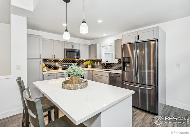 kitchen with sink, a kitchen island, dark hardwood / wood-style flooring, stainless steel appliances, and pendant lighting