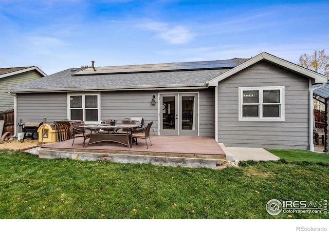 back of property featuring solar panels, a wooden deck, and a lawn