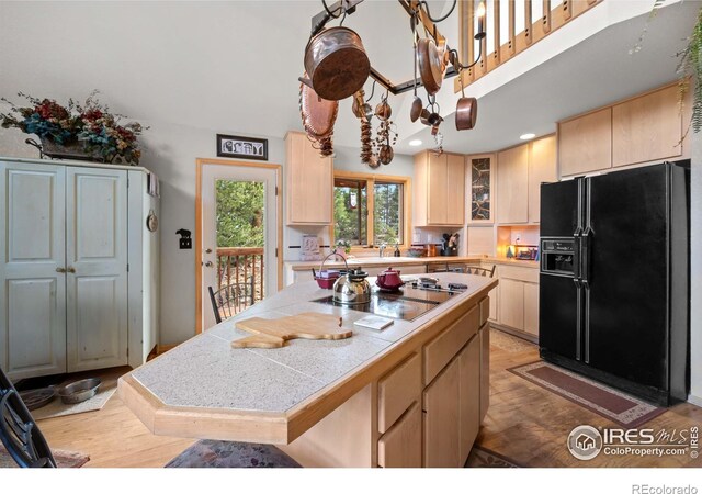 kitchen featuring light brown cabinets, a kitchen island, black fridge, cooktop, and light hardwood / wood-style floors