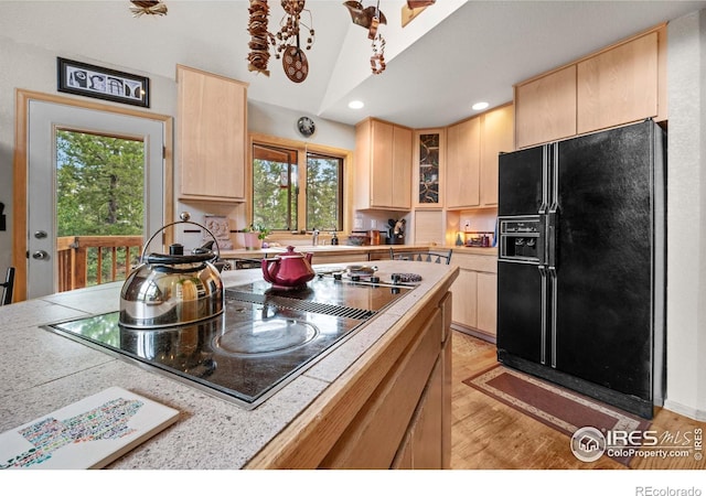 kitchen featuring light brown cabinets, vaulted ceiling, light hardwood / wood-style flooring, black appliances, and sink