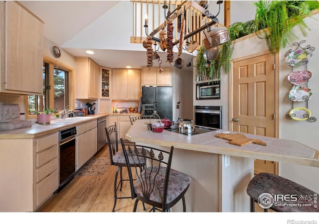 kitchen with light brown cabinets, stainless steel appliances, sink, a breakfast bar, and light hardwood / wood-style floors