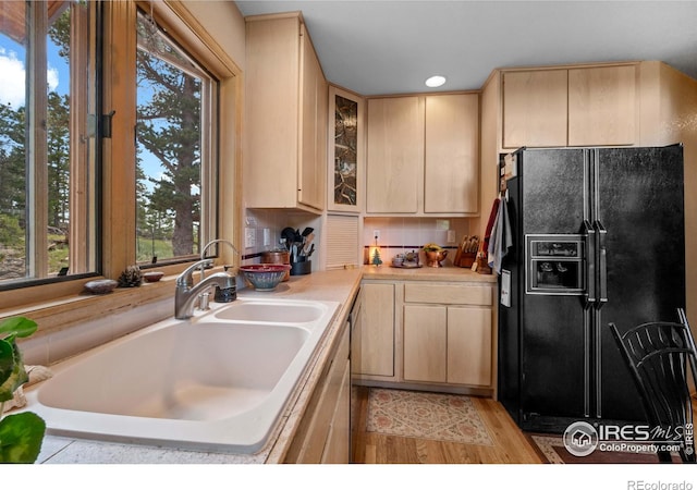 kitchen featuring light brown cabinetry, sink, light wood-type flooring, and black fridge