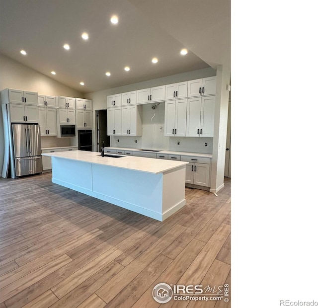 kitchen with a center island with sink, a sink, light wood-style floors, appliances with stainless steel finishes, and light countertops