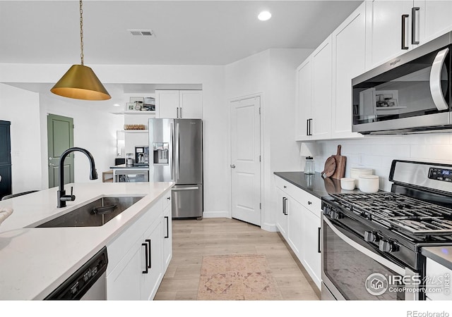 kitchen featuring appliances with stainless steel finishes, light wood-type flooring, sink, white cabinets, and hanging light fixtures