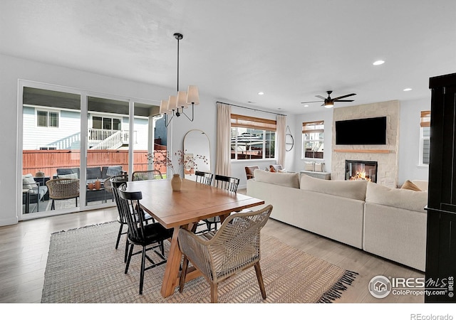 dining area with ceiling fan with notable chandelier, light wood-type flooring, and a large fireplace