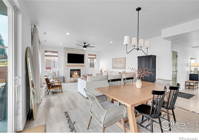 dining room featuring a large fireplace, ceiling fan with notable chandelier, and light hardwood / wood-style floors