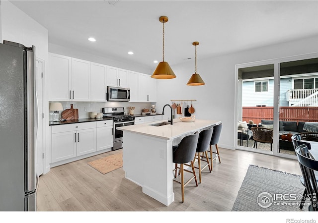 kitchen with a kitchen island with sink, sink, hanging light fixtures, light hardwood / wood-style flooring, and appliances with stainless steel finishes