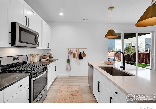 kitchen featuring sink, stainless steel appliances, light hardwood / wood-style floors, decorative light fixtures, and white cabinets