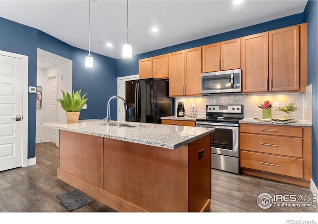 kitchen with appliances with stainless steel finishes, sink, hanging light fixtures, dark hardwood / wood-style floors, and a kitchen island with sink