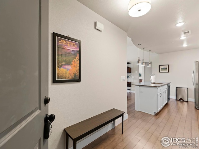 kitchen with appliances with stainless steel finishes, light wood-type flooring, an island with sink, hanging light fixtures, and white cabinetry