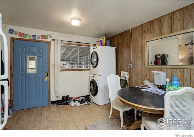 washroom featuring light wood-type flooring, stacked washer and clothes dryer, and wooden walls