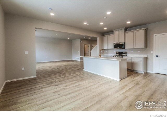 kitchen featuring appliances with stainless steel finishes, a kitchen island with sink, sink, and light wood-type flooring