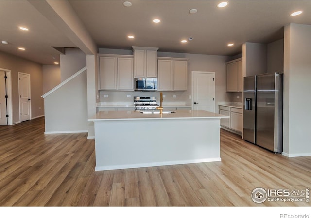 kitchen with an island with sink, appliances with stainless steel finishes, sink, and light wood-type flooring