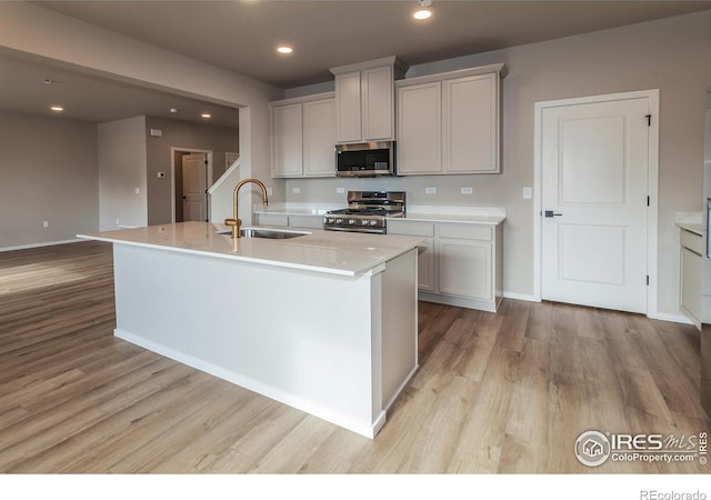 kitchen with appliances with stainless steel finishes, sink, an island with sink, and gray cabinetry