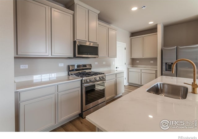 kitchen with light stone countertops, appliances with stainless steel finishes, sink, and dark wood-type flooring