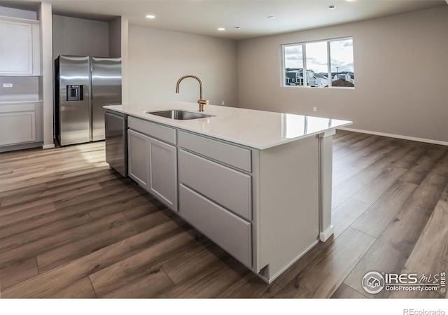 kitchen with dark hardwood / wood-style floors, appliances with stainless steel finishes, sink, and a kitchen island with sink