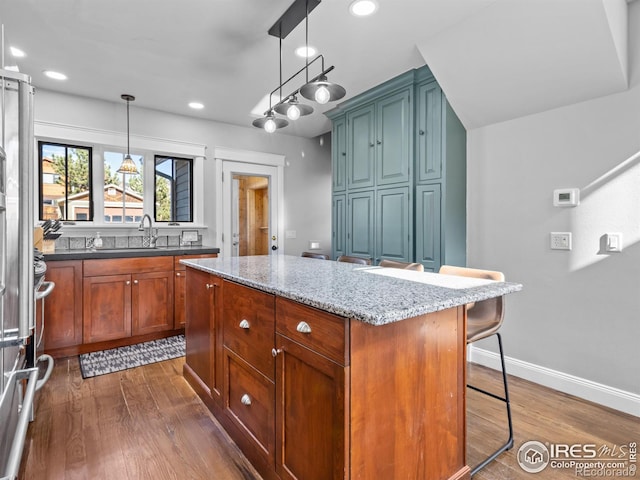 kitchen with light stone countertops, a kitchen island, pendant lighting, dark wood-type flooring, and a breakfast bar area