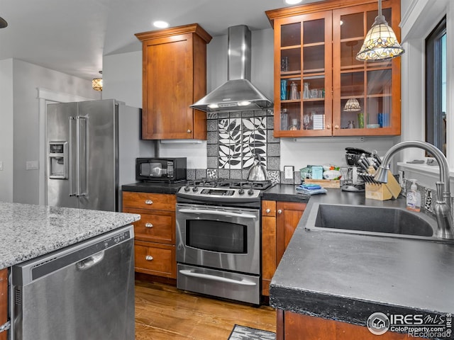 kitchen featuring wall chimney range hood, sink, appliances with stainless steel finishes, decorative light fixtures, and hardwood / wood-style flooring