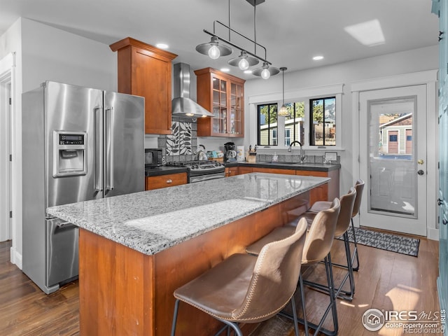 kitchen with a kitchen island, appliances with stainless steel finishes, wall chimney range hood, and dark wood-type flooring