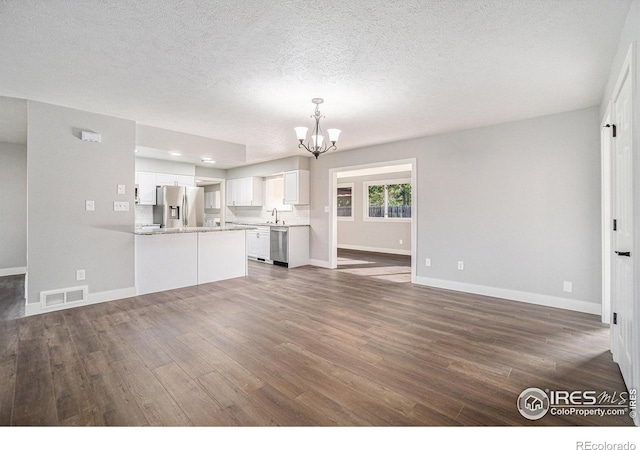 unfurnished living room featuring sink, dark wood-type flooring, a textured ceiling, and a chandelier