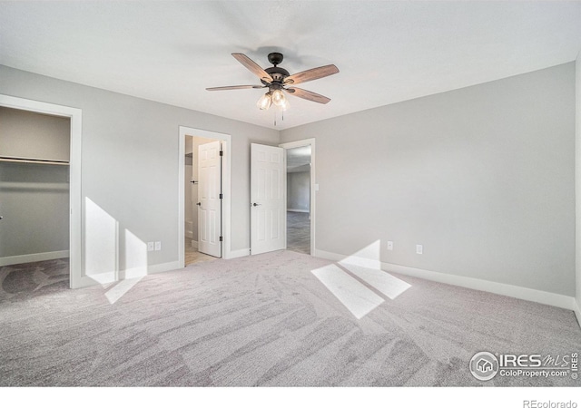 unfurnished bedroom featuring a closet, ceiling fan, light carpet, and a walk in closet