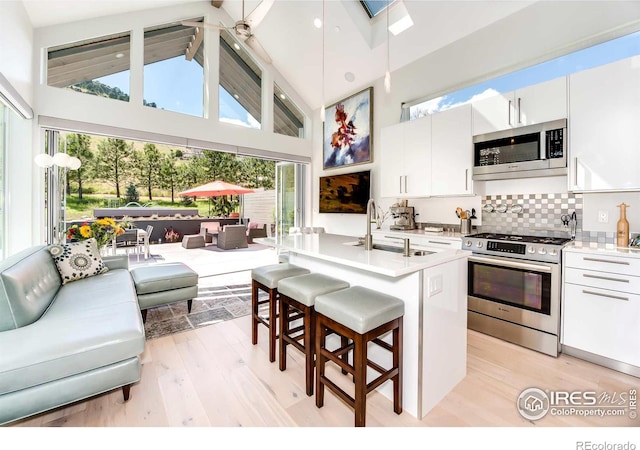 kitchen with stainless steel appliances, sink, light wood-type flooring, white cabinetry, and high vaulted ceiling