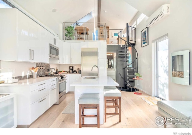 kitchen featuring appliances with stainless steel finishes, light wood-type flooring, white cabinetry, a wall mounted AC, and a center island with sink