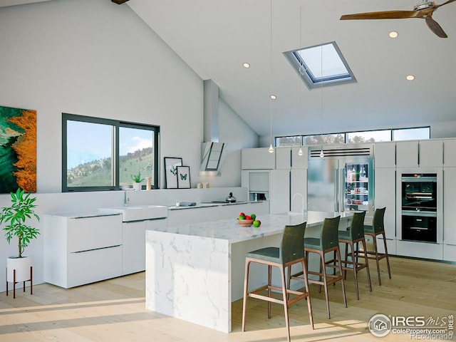 kitchen with a kitchen breakfast bar, sink, light wood-type flooring, white cabinets, and high vaulted ceiling