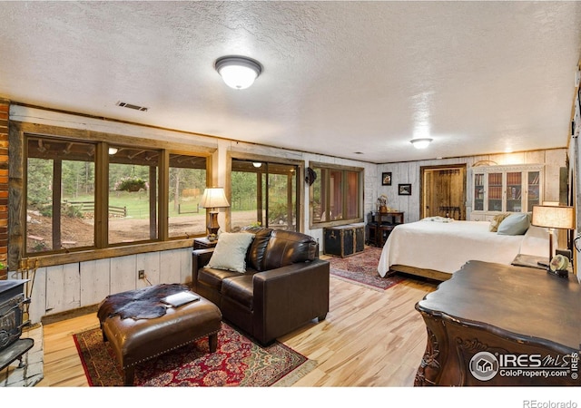 bedroom with light hardwood / wood-style flooring, a textured ceiling, and wood walls