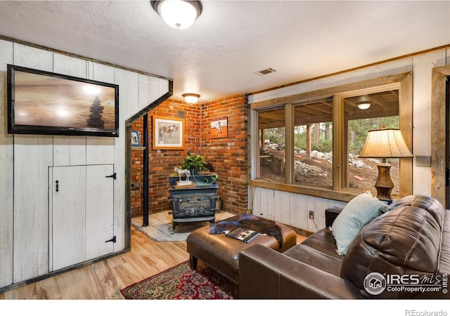 living room featuring wood walls, light wood-type flooring, a wood stove, a textured ceiling, and brick wall