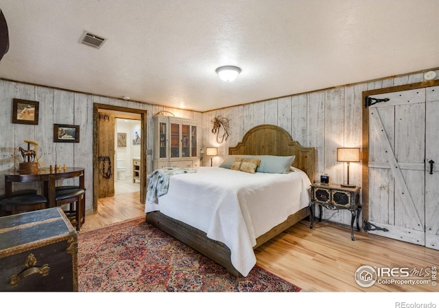 bedroom featuring wood walls, hardwood / wood-style floors, and ensuite bath