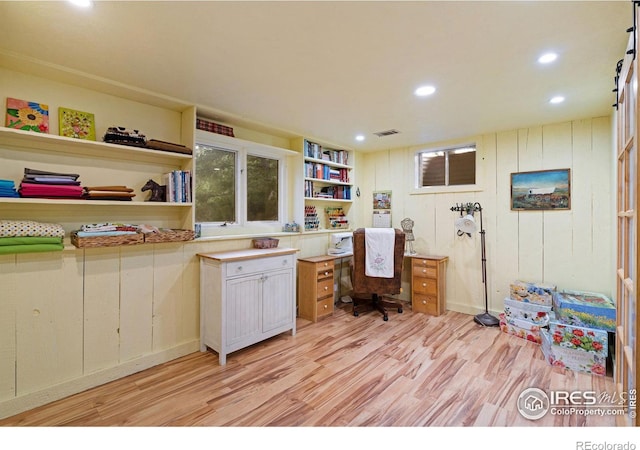 home office featuring built in desk, light wood-type flooring, and a barn door