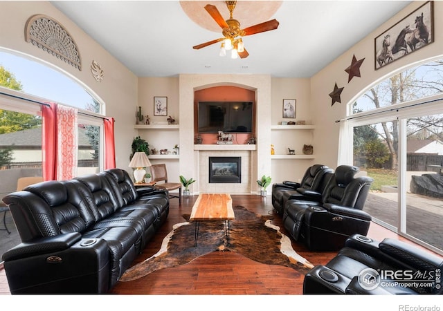 living room with a tiled fireplace, ceiling fan, wood-type flooring, and plenty of natural light