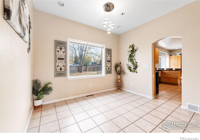 tiled spare room featuring a notable chandelier