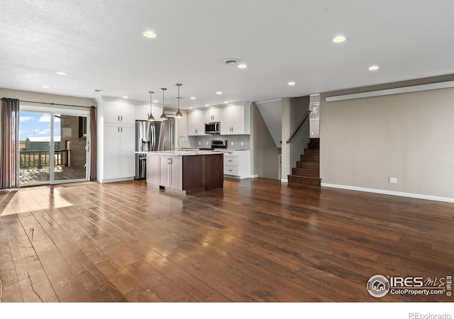 kitchen with decorative light fixtures, white cabinets, an island with sink, and stainless steel appliances