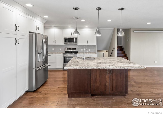 kitchen featuring a center island with sink, white cabinetry, hanging light fixtures, appliances with stainless steel finishes, and dark wood-type flooring