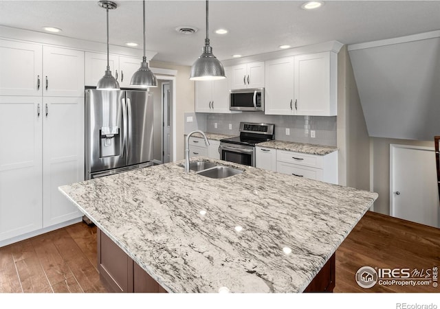 kitchen featuring stainless steel appliances, white cabinetry, decorative light fixtures, and an island with sink