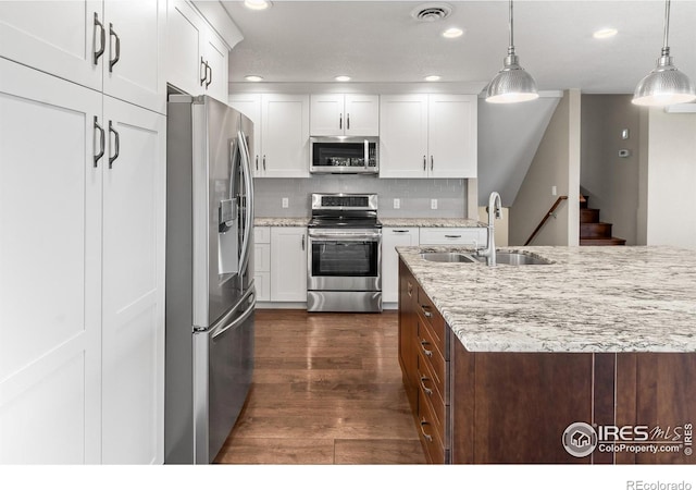 kitchen with hanging light fixtures, white cabinets, appliances with stainless steel finishes, and sink