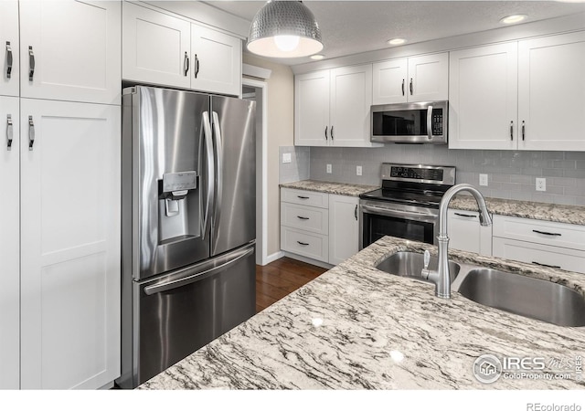 kitchen featuring white cabinetry, appliances with stainless steel finishes, decorative backsplash, light stone counters, and sink