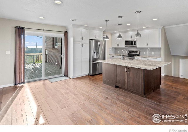 kitchen with light stone counters, white cabinetry, stainless steel appliances, and a kitchen island with sink