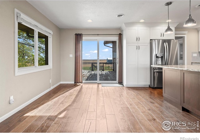 kitchen featuring hardwood / wood-style floors, stainless steel refrigerator with ice dispenser, pendant lighting, white cabinets, and light stone counters