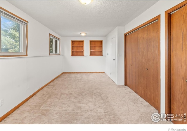 carpeted spare room with a textured ceiling and built in shelves