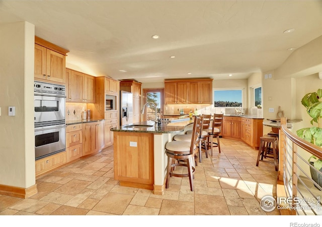 kitchen with plenty of natural light, a kitchen island with sink, double oven, and sink