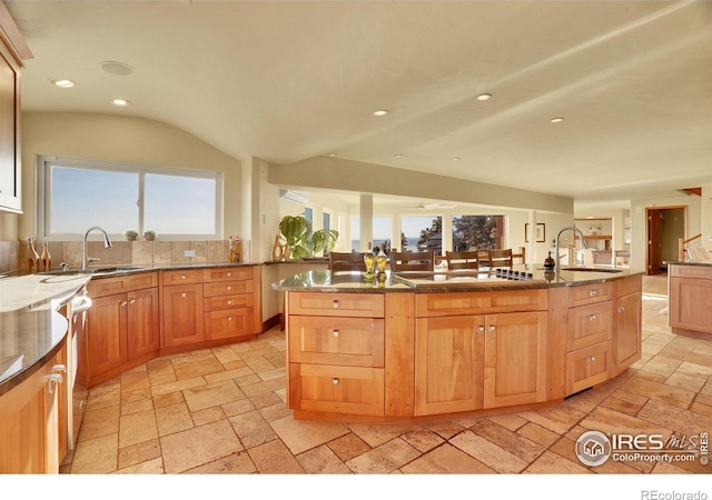 kitchen featuring sink, backsplash, cooktop, and an island with sink