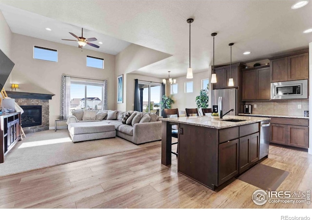 kitchen with an island with sink, light hardwood / wood-style flooring, stainless steel appliances, decorative light fixtures, and light stone counters