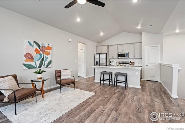 kitchen featuring gray cabinetry, a center island with sink, stainless steel appliances, a kitchen breakfast bar, and lofted ceiling